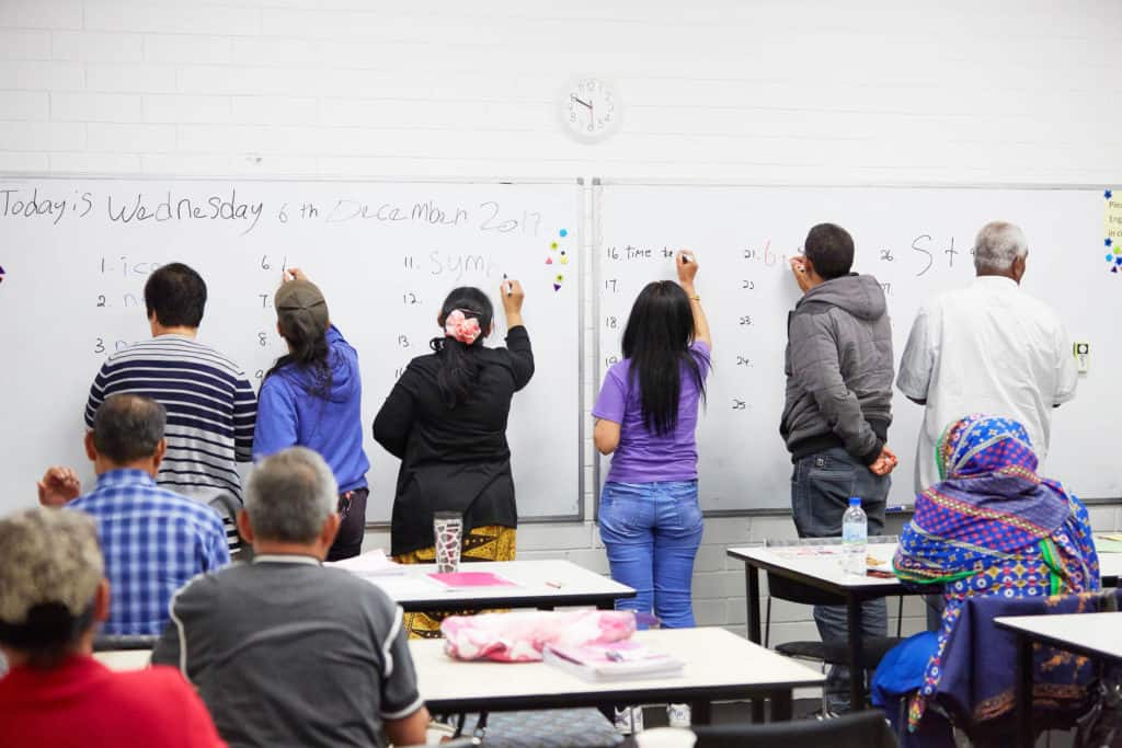 six students writing on white board in classroom
